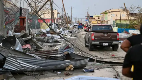 AFP via Getty Images A car drives through the a destroyed neighbourhood following the passage of Hurricane Melissa, in Black River, Jamaica