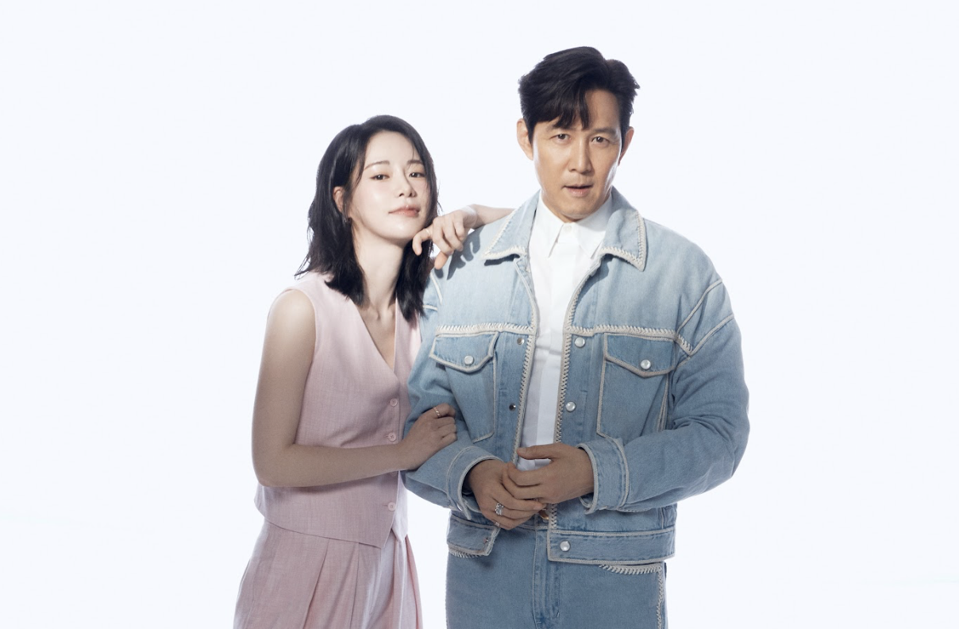 A woman in a pink suit leans on the shoulder of a man wearing denim.