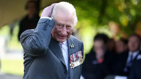 Getty Images King Charles III wears a grey blazer emblazonsed with service medals during the dedication ceremony for a new memorial to the Armed Forces LGBT+ community at Founders Room National Memorial Arboretum on October 27, 2025 in Alrewas, Staffordshire. 
